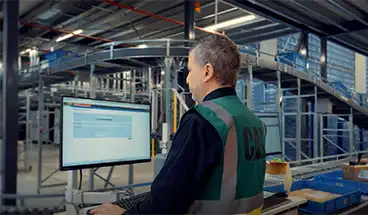 Un homme derrière un écran WMS dans un entrepôt logistique